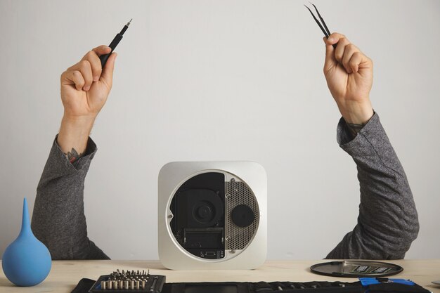 Free photo a man's hands with pincers and screwdriver, the man's head is hidden behind a computer, on white wall