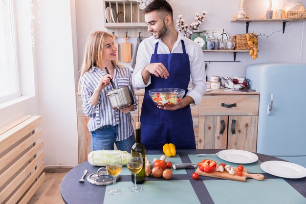 Man salting salad while woman mixing food in pot