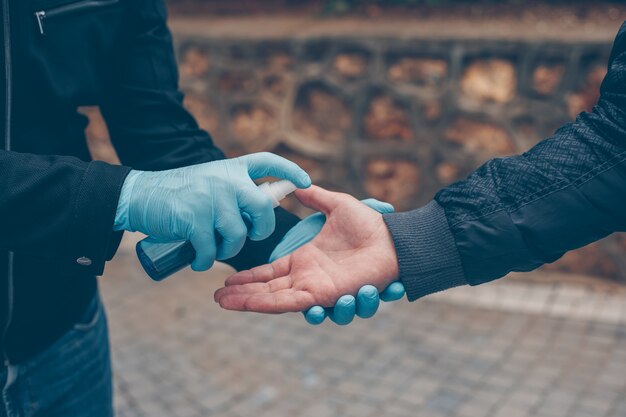 A man sanitizing other one's hand in gloves in yard during daytime .  