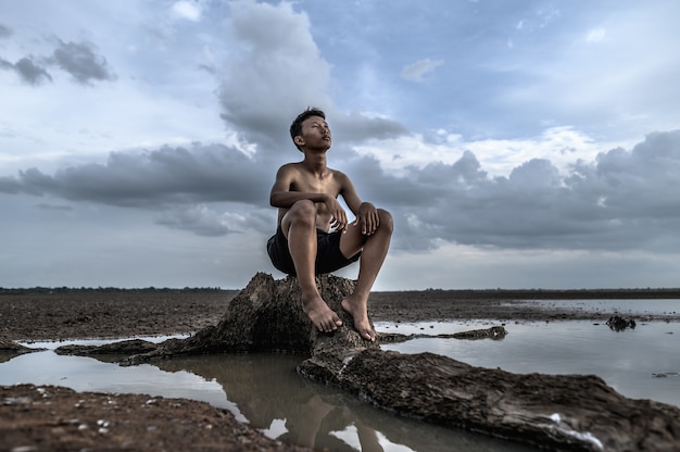 A man sat bent his knees, looking at the sky at the base of the tree and surrounded by water.