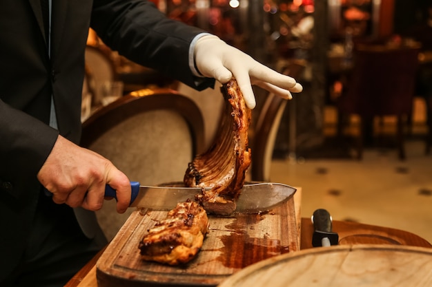 Man separates grilled ribs on the wooden board side view