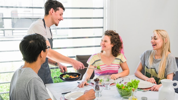 Man serving fresh cooked vegetables to her female friends at home