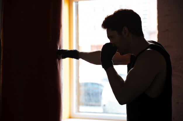 Free photo man in shadow kicking the punching bag