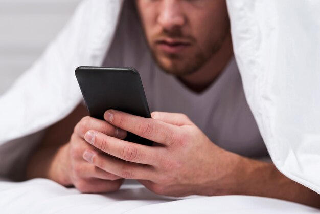 Man behind sheets checking his phone