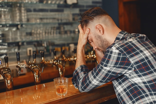 シャツを着た男がグラスを手に持っています。男はバーに座って頭を抱えています。