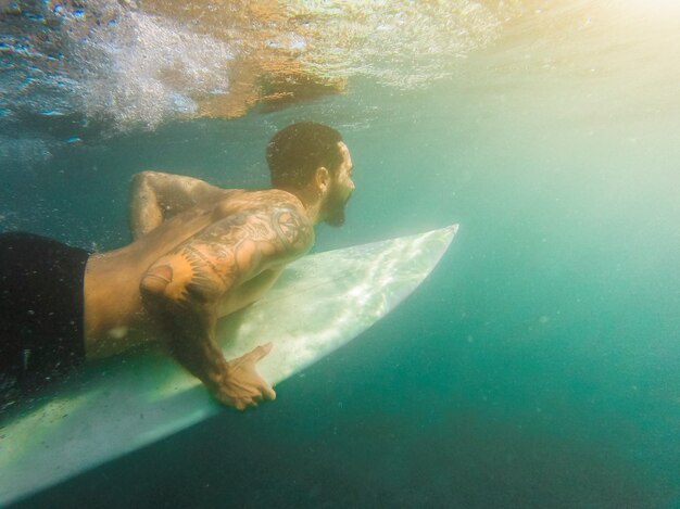 Man in shorts diving with surfboard underwater