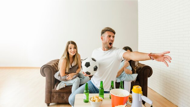 Man shouting watching football match with friends on sofa