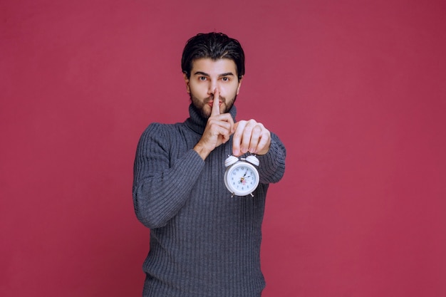 Man showing the alarm clock and asking for silence. 