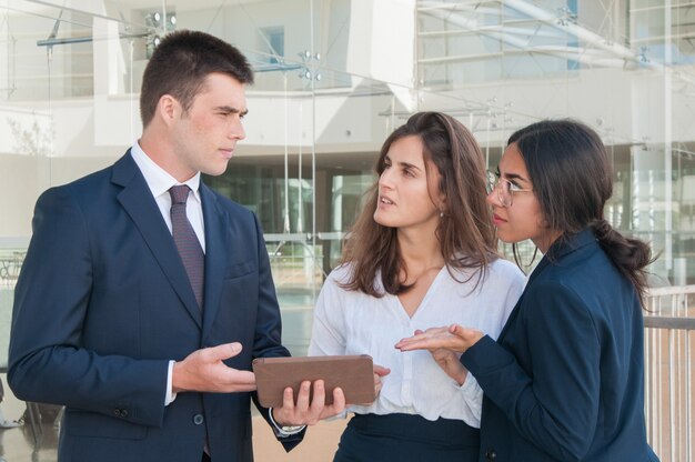 Man showing colleagues data on tablet, they looking uncertain