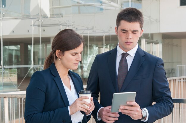 Man showing data on tablet, woman looking, holding coffee 