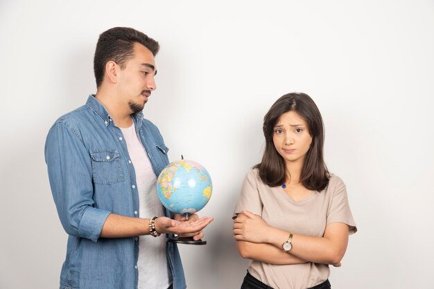 Человек показывает земной шар рядом с обиженной девушкой.