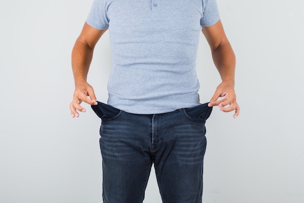 Человек показывает пустые карманы в серой футболке, джинсах