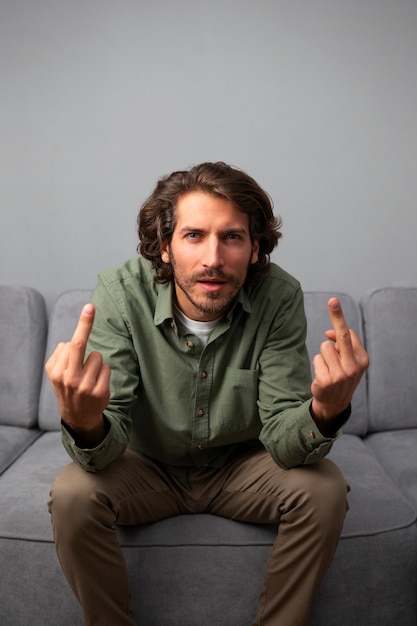 Free photo man showing middle finger while sitting on the sofa