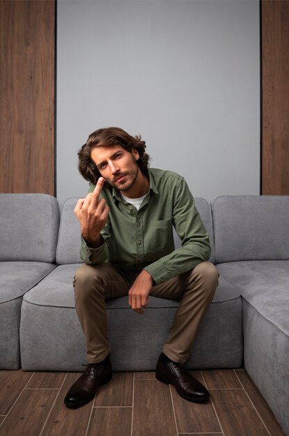 Мужчина показывает средний палец, сидя на диване