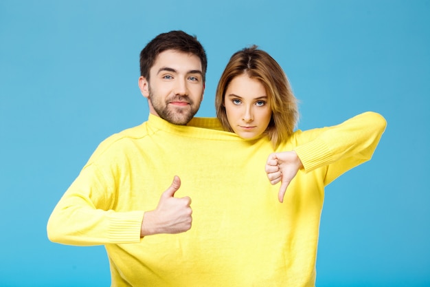 Man showing okay girl guestering thunb down over blue wall