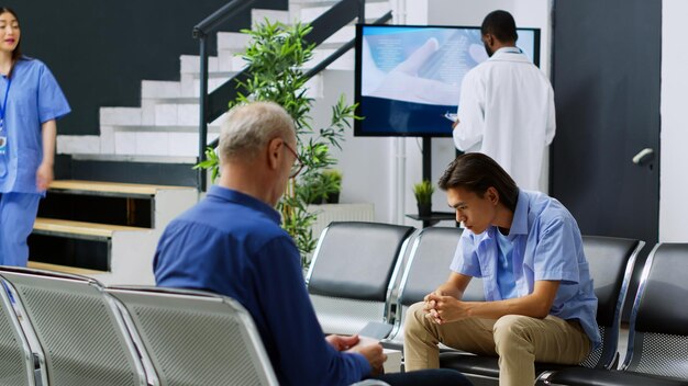 A man sits in a chair with a man in a blue shirt and a woman in a white shirt.