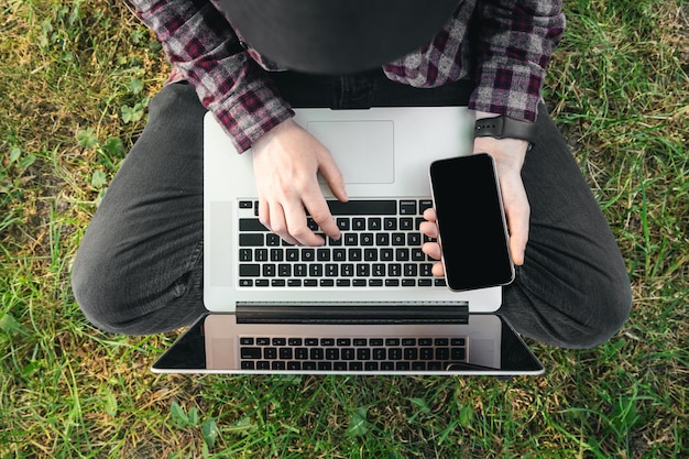 Foto gratuita un uomo si siede sull'erba con una vista dall'alto di un laptop e uno smartphone