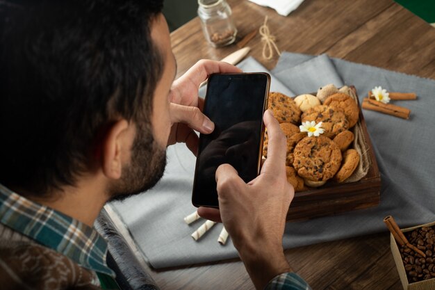 クッキーテーブルの周りに座って、彼の電話で遊ぶ男