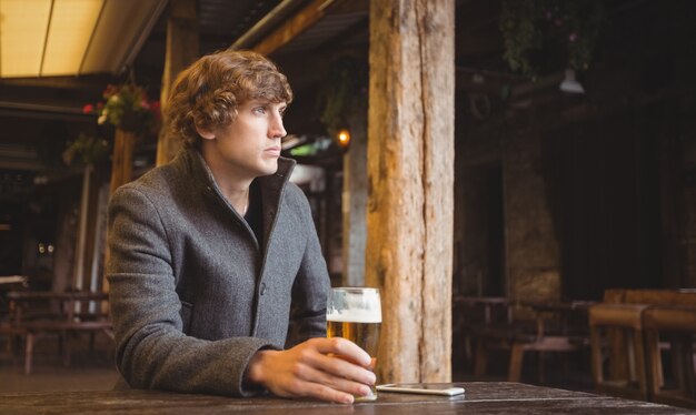 Человек сидит в баре с бокалом пива на столе