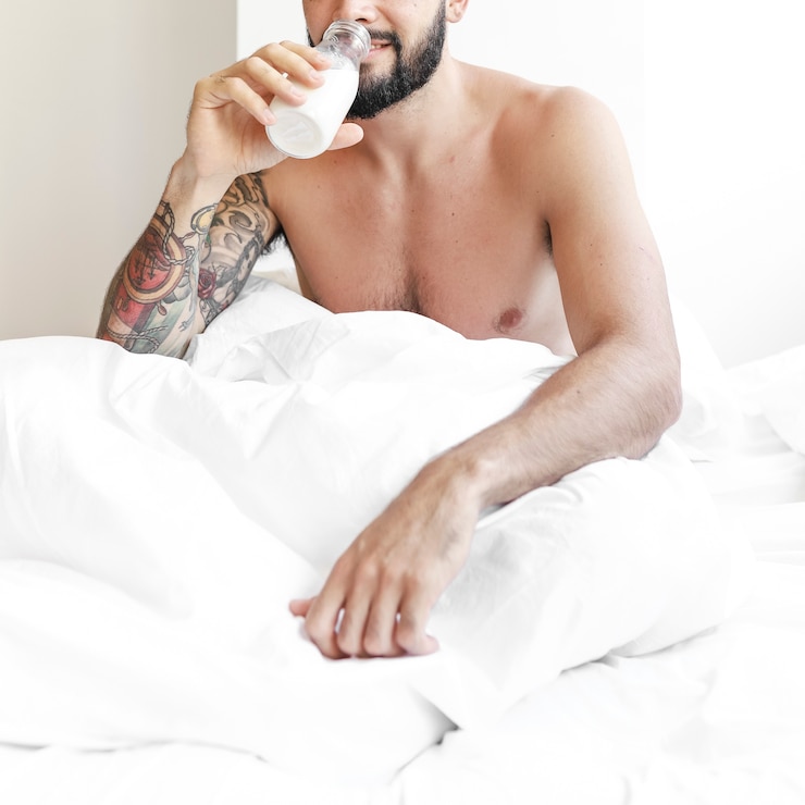 Free Photo man sitting on bed drinking milk