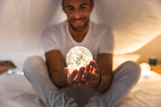 Man sitting on bed holding glowing sphere in two hands