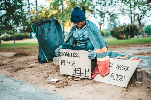 A man sitting beggars with homeless please help message.