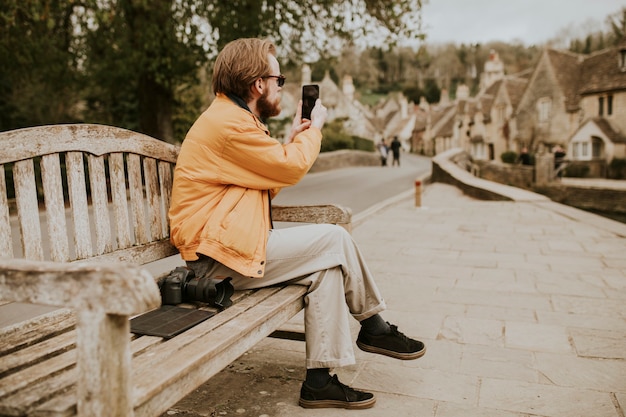 ベンチに座って、村で彼の携帯電話で写真を撮る男