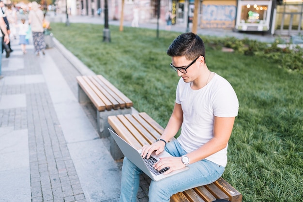 Man sitting on bench working on laptop