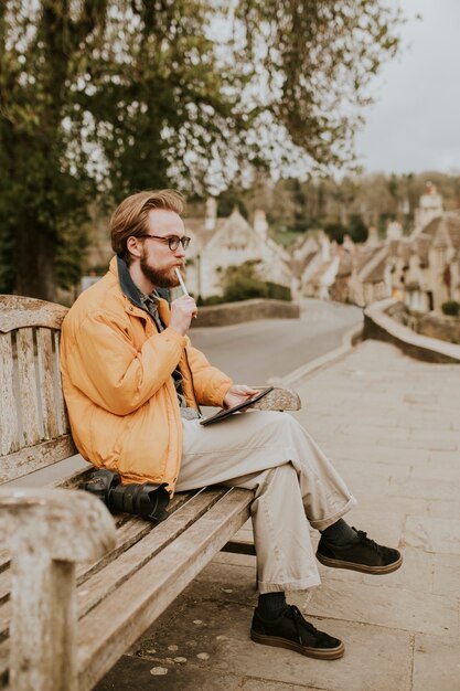 Free photo man sitting on a bench and working on tablet in the village