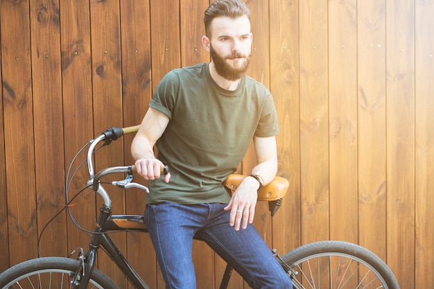 Man sitting on bicycle against wooden backdrop