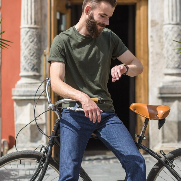 腕時計で時間を見て自転車に座っている男