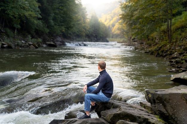 Foto gratuita uomo seduto vicino alla vista laterale del fiume