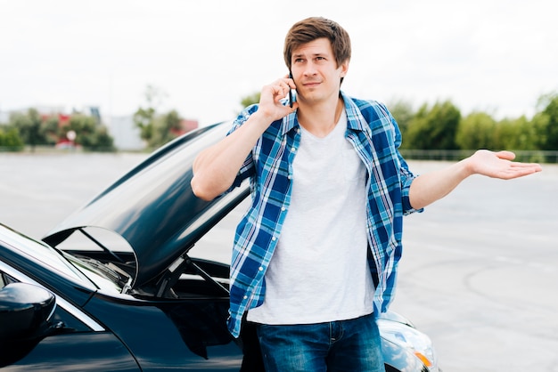 Man sitting on car and talking on phone