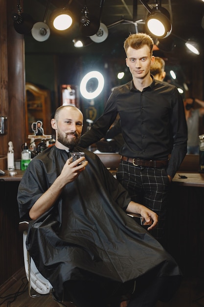 Man sitting in a chair. Hairdresser with a client. Guy drinkig a whiskey.
