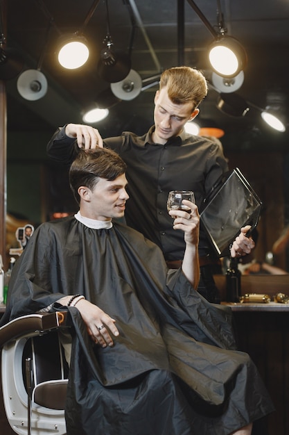 Man sitting in a chair. Hairdresser with a client. Guy drinkig a whiskey.