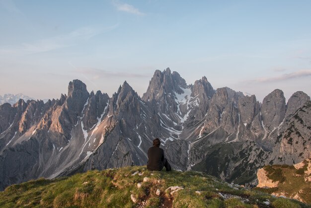 灰色の山に面した崖の上に座っている男