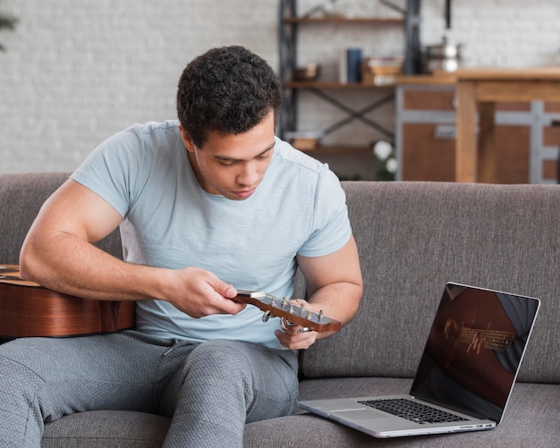 Man sitting on couch and tuning the guitar