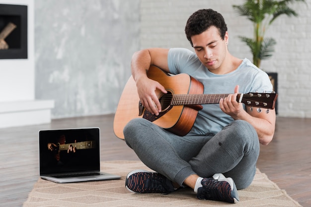 Мужчина сидит на полу и учится играть на гитаре