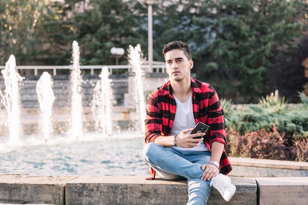 Man sitting in front of fountain holding smartphone