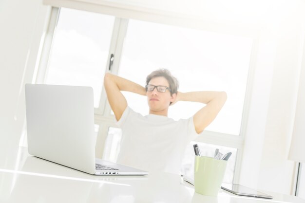 Man sitting in front of laptop with hands behind head