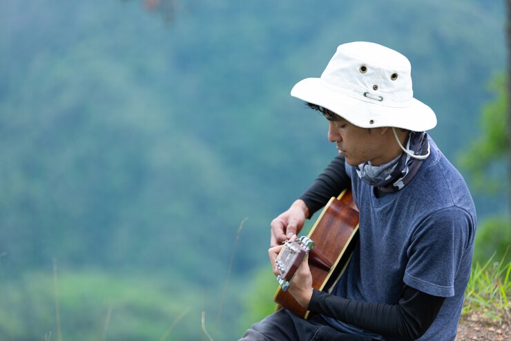 Free Photo a man sitting happily playing guitar in the forest alone.