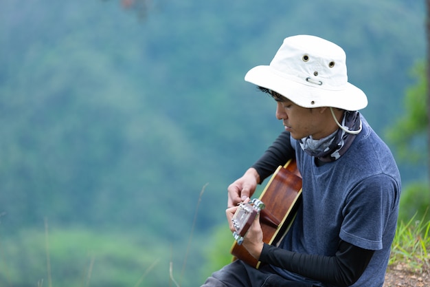 A man sitting happily playing guitar in the forest alone.