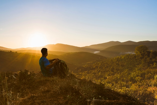 夕日の風景で丘の上に座っている男