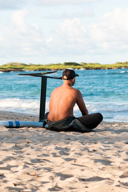 Man sitting next to his surfing board outdoors