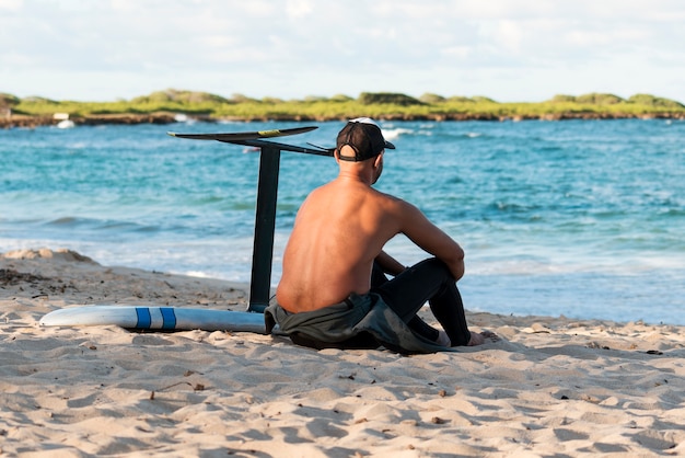 Man sitting next to his surfing board outdoors