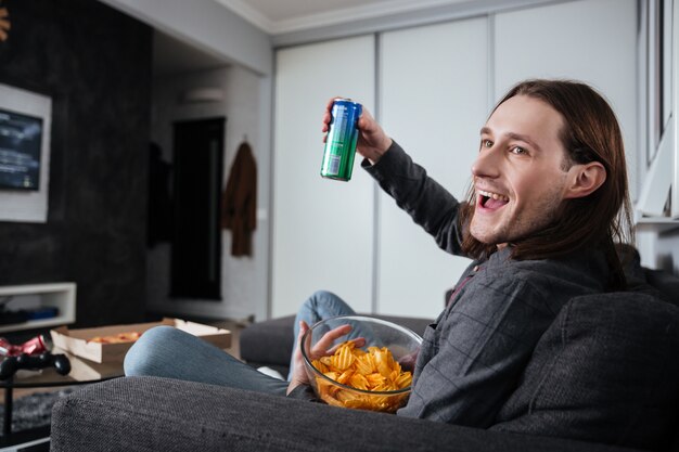 屋内でポテトチップスを食べて家で座っている男はテレビを見る