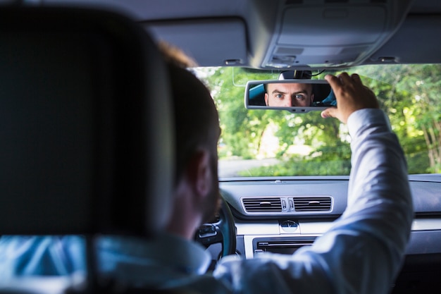 Man sitting inside car adjusting rear view mirror. 