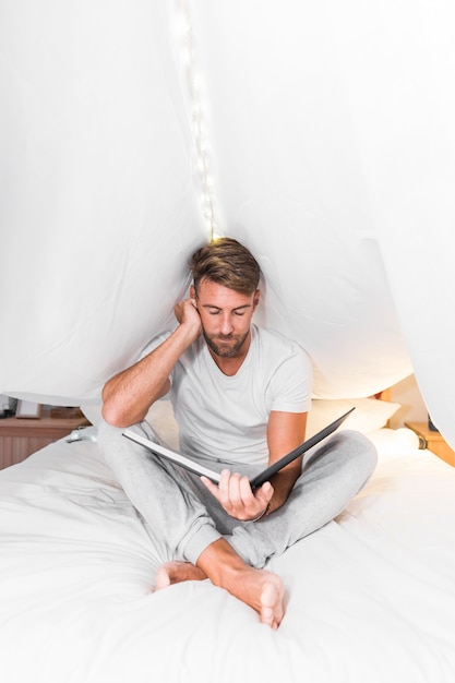 Man sitting inside the curtain looking at photo album on bed