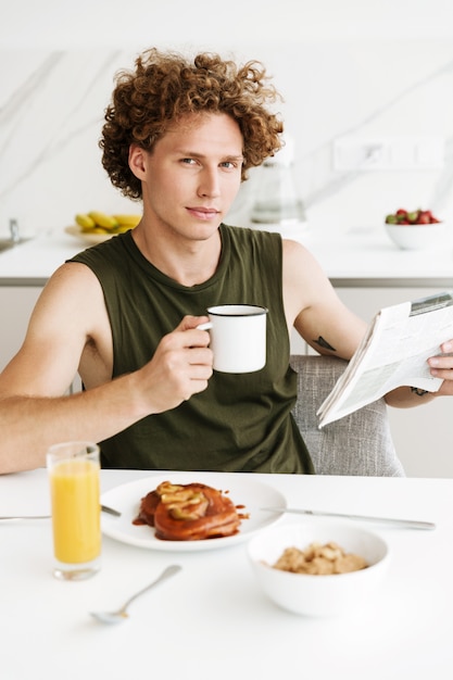 Мужчина сидит на кухне, держа газету