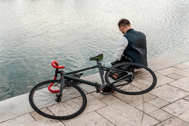 Free photo man sitting next to a lake with his bike